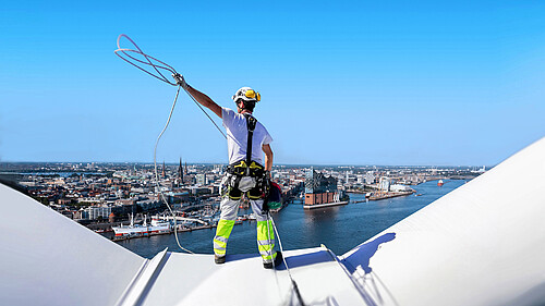 WindEnergy Header Mann von Hinten auf einem Windrad mit Stadtblick