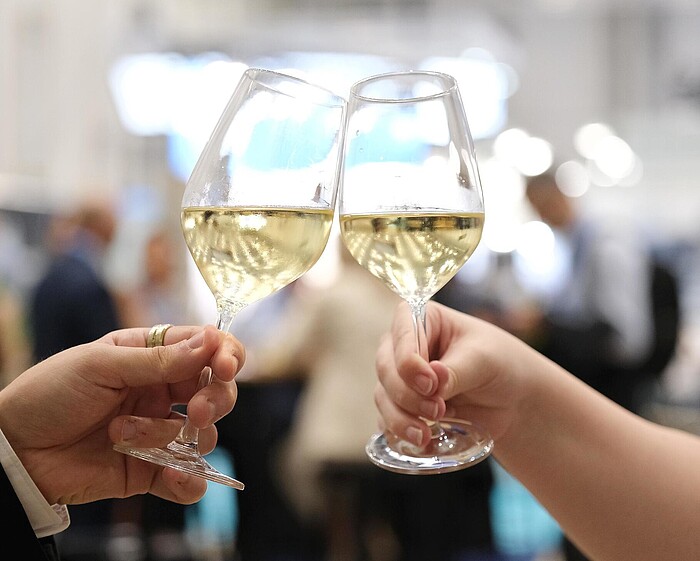 Nahaufnahme von zwei Weingläsern in jeweils einer weiblichen und männlichen Hand, die anstoßen.